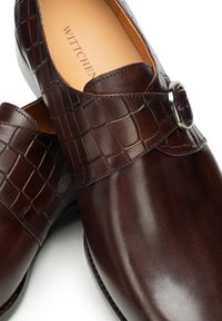 Braune Lederschuhe mit einem Riemen im Krokodilmuster und silbernen Metallakzenten. Glatte Textur und gerundetes Zehendesign, mit subtilem Glanz.