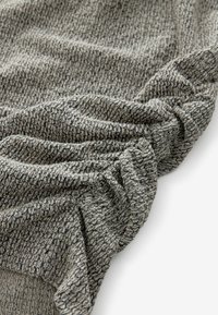 Tissu tricoté texturé dans des tons de gris, présentant un design froissé avec des motifs contrastants subtils, d'apparence douce et drapée.