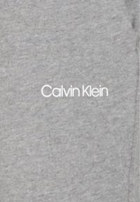 Grau Baumwollstoff T-Shirt mit einem weißen "Calvin Klein" Logo, das sich vorne in der Mitte befindet. Glatte Textur mit klassischem Schnitt.
