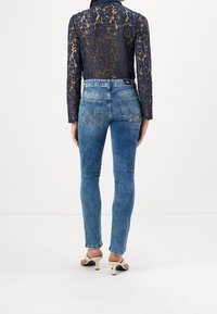 Haut en dentelle noire à manches longues associé à un jean skinny bleu clair. Le jean présente un design cinq poches avec des poches arrière ornées de détails de couture.