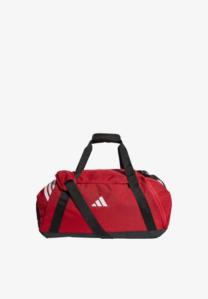 Czerwona sportowa torba typu duffel z czarnymi paskami, białym logo Adidas oraz białymi paskami z jednej strony, przedstawiona na białym tle.