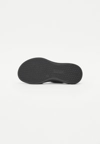 Black rubber shoe sole with textured pattern featuring small squares. Rounded shape with slight curvature at the toe area.