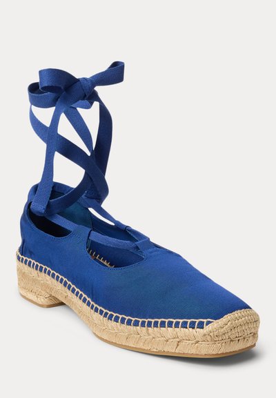 Plavi platneni espadril ravni s pletenim potplatom od juta i trakama za vezanje oko gležnja vezanim u mašnu.