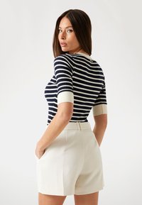 Navy and white striped fitted top with short sleeves, paired with cream shorts, featuring a clean design and side pockets.