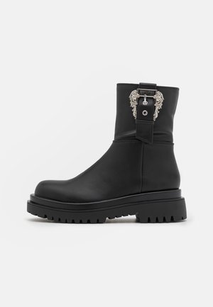 Schwarzer Stiefel bis zur Mitte der Wade mit dicker Profilsohle und dekorativer silberner Schnalle mit filigranen Details an der Außenseite.