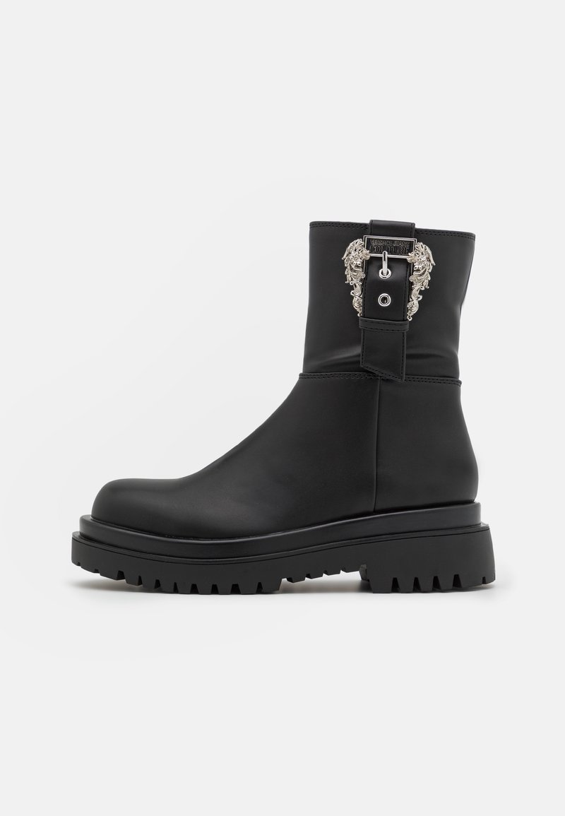 Botte noire mi-mollet avec semelle épaisse à crampons et boucle argentée décorative présentant des détails élaborés sur le côté extérieur.