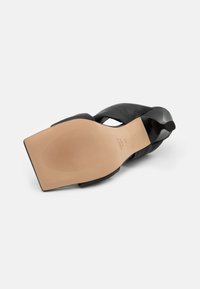 Sandal com salto alto preto, com parte superior em couro liso, bico aberto, tiras cruzadas e sola de borracha castanha com ranhuras horizontais para tração.