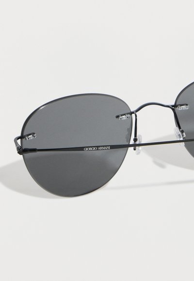 Στρογγυλά γυαλιά ηλίου Giorgio Armani με μαύρο σκελετό, σκουρόχρωμους γκρι φακούς και ρυθμιζόμενα μαξιλαράκια στη μύτη σε λευκό φόντο.
