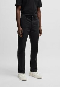 Pantaloni negri din bumbac cu croială dreaptă, design cu cinci buzunare și închidere cu nasture. Purtați cu adidași albi.
