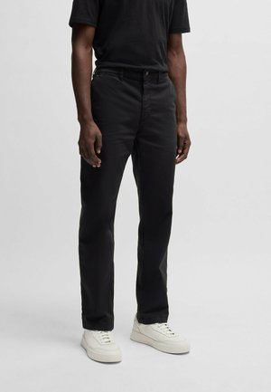 Black cotton trousers with a straight fit, five-pocket design, and a button closure. Worn with white sneakers.
