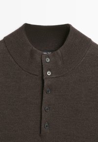 Primo piano di un maglione a maglia marrone scuro con colletto alto a coste e una fila verticale di cinque bottoni neri sul davanti.