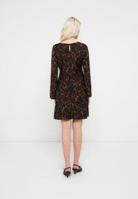 Rochie neagră cu imprimeu leopard maro, mâneci lungi și detaliu la spate în formă de cheie, realizată din material ușor. Purta cu sandale negre.