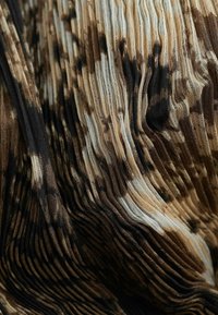 Tissu texturé avec des plis dans des tons de marron, beige et noir. Présente un motif de largeurs et de lignes variées, créant un effet ondulé.