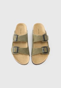 Sandales en daim vert olive avec deux brides ajustables et boucles en argent. Semelle intérieure beige douce avec une semelle extérieure foncée contrastante. Design décontracté.