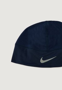 Sötétkék, puha anyagból készült sapka, díszített varrással és egy fényvisszaverő szürke Nike logóval az elején. Kiválóan alkalmas szabadtéri tevékenységekhez.