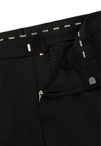 Black trousers with a smooth fabric, featuring a front zipper, internal tag with “BOSS” logo, and a sleek design.