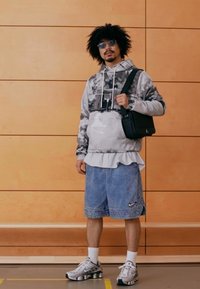 Sportos öltözék, szürke terepmintás kapucnis pulóverrel, fehér bordázott szegéllyel rétegezve, kék farmer rövidnadrággal, melyen Nike logó látható, és ezüst sportcipőkkel.