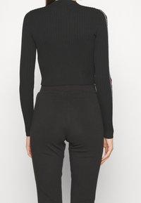 Černý žebrovaný crop top s dlouhými rukávy, s přiléhavým střihem a decentním výstřihem do V. Jednoduchá textura bez viditelných vzorů nebo kovových prvků.