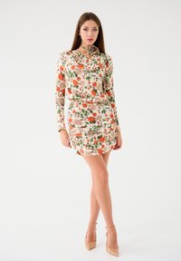 Kwiatowa sukienka z długimi rękawami, z kremowym tłem i różowo-pomarańczowymi różami. Materiał jest gładki, o dopasowanej sylwetce i marszczonym detalu.