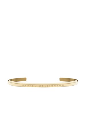 Kovový náramek tónovaný do zlaté s otevřenými konci a rytým nápisem "DANIEL WELLINGTON" na vnější straně.