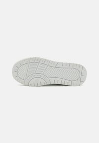Biała gumowa podeszwa sneakersów z teksturowanym gripem, z wzorami w zygzaki oraz okrągłym logo. Czysty design z minimalnymi zdobieniami.