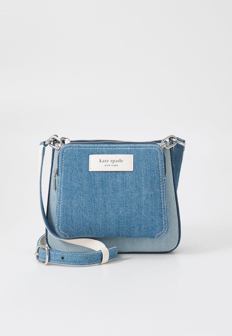 Denim crossbody bag with a blue gradient design, silver hardware, and a white logo patch. Features an adjustable strap and zip closure.