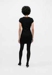 Μαύρο εφαρμοστό φόρεμα με υφασμάτινο πλεκτό σχέδιο, κοντά μανίκια και στρογγυλεμένο ντεκολτέ. Φορεμένο με μαύρες καλσόν και μυτερές γόβες.