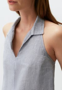 Blusa senza maniche di colore grigio chiaro realizzata in lino. Caratterizzata da un colletto, scollatura aperta e una texture sottile con una vestibilità rilassata.