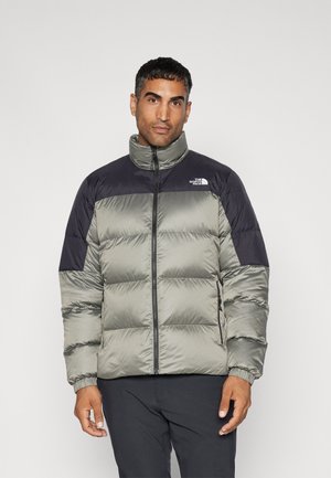 Giacca a vento con corpo verde oliva chiaro e spalle nere, chiusura a zip, polsini a coste e logo North Face sul petto.