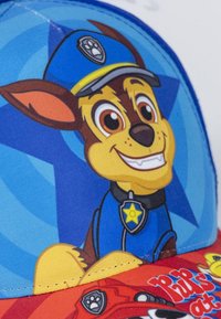 Cappello da baseball con un personaggio di cartone di un cane che indossa una divisa e un cappello blu, su uno sfondo blu e rosso con grafiche giocose.