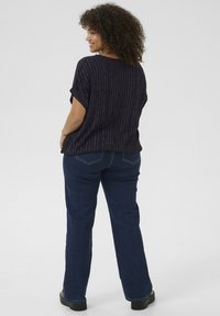 Blouse marine avec des rayures verticales argentées et des manches retroussées, associée à un jean droit bleu foncé et des chaussures noires.