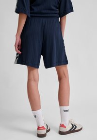 Mörkblå shorts med ribbad textur, avslappnad passform, sidostripes och midjeband. I kombination med vita strumpor och beiga sneakers med röda detaljer.