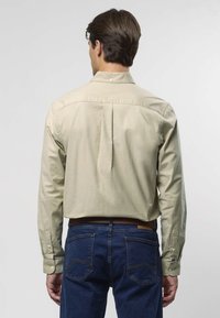 Hellbeiges Hemd mit Knopfleiste und langen Ärmeln, mit einer Rückenfalte und Kragen, kombiniert mit dunkelblauen Jeans, die Gesäßtaschen zeigen.