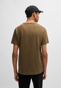 Brown cotton t-shirt with short sleeves and a round neckline, worn with a black baseball cap. Smooth texture, simple design, and relaxed fit.