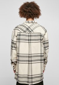 Beige rutete skjorte med svarte linjer, knapper på mansjettene og detalj ved ryggen. Laget av mykt materiale med en løs passform.