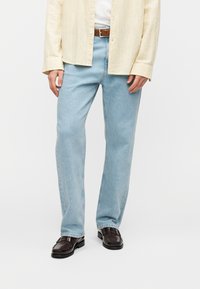 Ανοιχτό μπλε τζιν με ίσια γραμμή, διαθέτοντας κλασικό σχέδιο με πέντε τσέπες και απλό τελείωμα. Φορεμένο με σκούρα καφέ παπούτσια.