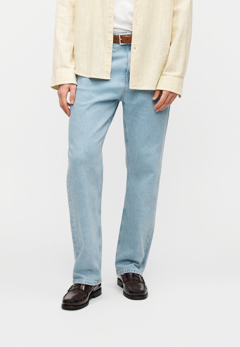 Ανοιχτό μπλε τζιν με ίσια γραμμή, διαθέτοντας κλασικό σχέδιο με πέντε τσέπες και απλό τελείωμα. Φορεμένο με σκούρα καφέ παπούτσια.