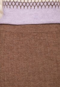 Gros plan d'une personne portant une jupe marron côtelée et un pull lavande avec un motif en losange marron près de l'ourlet.