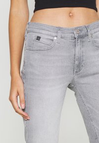 Šedé džínsy v úzkém střihu, s klasickým pětipocket uspořádáním, zapínáním na knoflík a decentním logem na přední kapse.