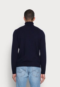 Marinblå polotröja i fint stickat material med en figurnära design. Har ribbade ärmslut och nederkant som kompletterar avslappnade jeans.