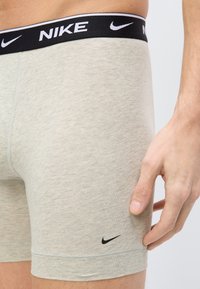 Κοντινή λήψη ενός ατόμου που φοράει ανοιχτό γκρι μπόξερ της Nike με μαύρη μέση και μικρό μαύρο λογότυπο Nike κοντά στο τελείωμα.