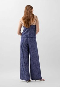 Ensemble à deux pièces bleu marine comprenant un haut à fines bretelles et un pantalon large avec un motif floral texturé. Tissu lisse et coupe décontractée.
