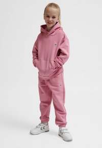 Rosa hoodie och matchande joggers i mjukt tyg. Huva med känguruficka. Med logotypdetalj på bröstet. Vita sneakers.