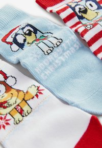 Trois paires de chaussettes colorées et à motifs mettant en scène des chiens de dessin animé en tenue de fête. Matériaux : tissu tricoté. Couleurs : bleu, blanc, rouge et rayé.