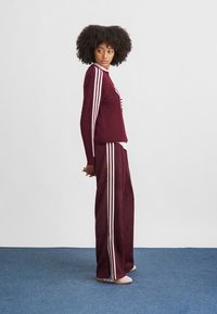 Conjunto de suéter e calças em malha bordeaux com riscas brancas nas mangas e laterais. Corte solto; a textura parece suave e aconchegante. Design de decote simples.