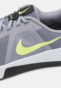 Sive tenisice za sport s mrežastim gornjim dijelom, žutom Nike swoosh logom, plastičnim detaljima i crnim gumiranim potplatom s izrezima za prianjanje.