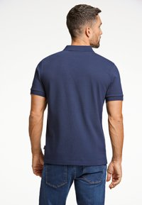 Marinblå polo-shirt med ribbad krage och korta ärmar, parat med denimjeans. Slät textur och figurnära design, synliga sömnadsdetaljer.