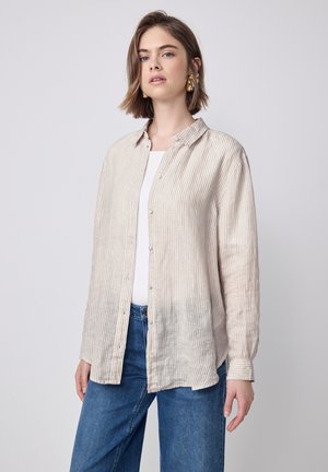Chemise boutonnée à rayures de couleur claire avec des manches longues, fabriquée en tissu doux. Dotée d'un col et d'une coupe décontractée, elle est associée à un jean bleu.