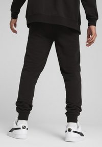 Pantaloni della tuta neri realizzati in tessuto morbido, con gambe affusolate e polsini a coste. Abbinati a sneaker bianche con strisce nere.