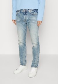 Ljusblå denimjeans med en urtvättad look och subtila slitningar. I kombination med vita sneakers och en ljusblå långärmad skjorta.
